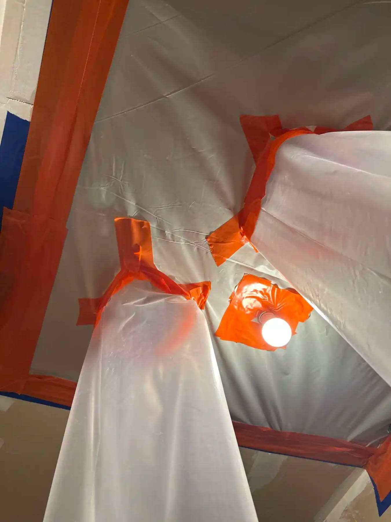 Plastic containment taped over a ceiling with a work light shining through