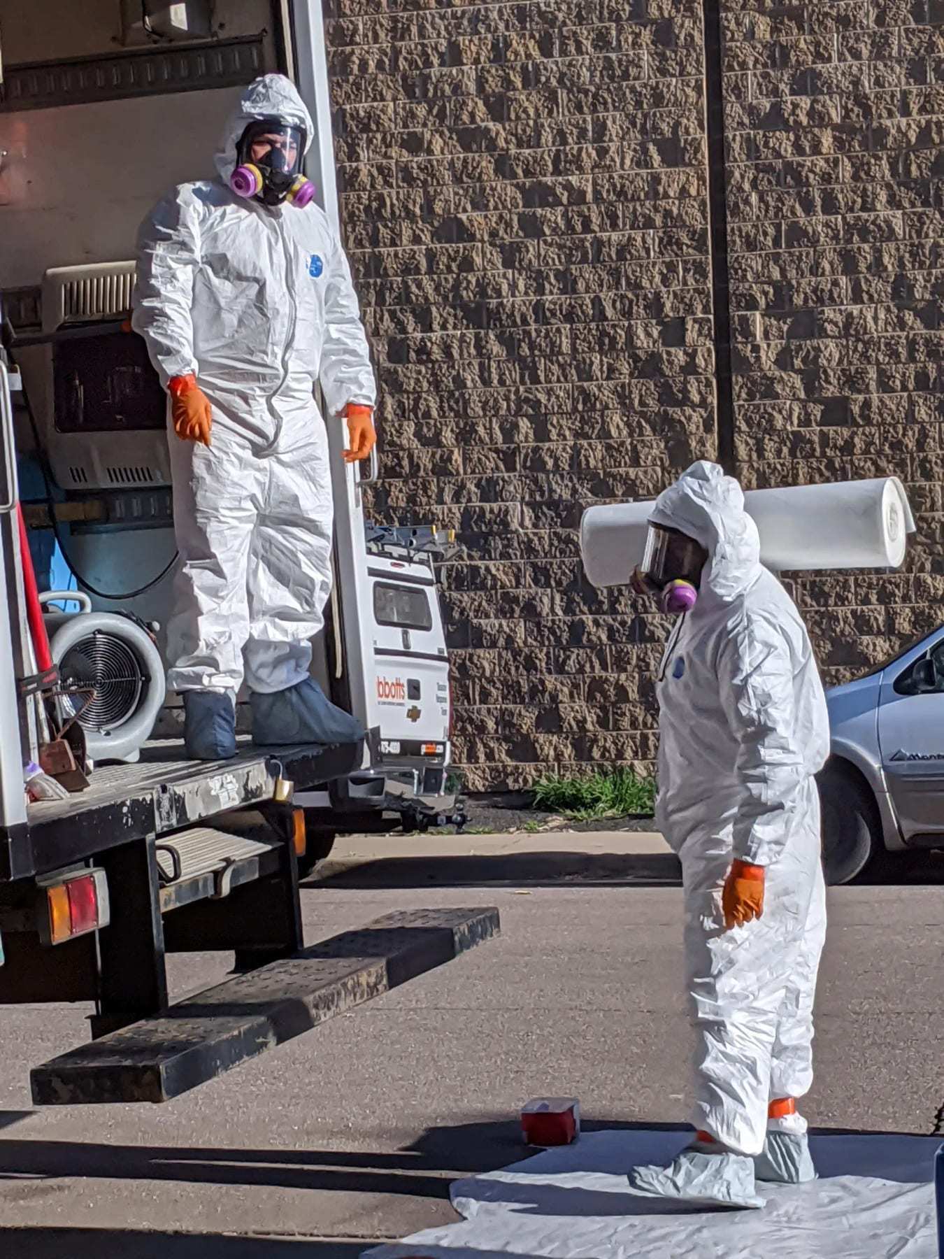 Two technicians in protective suits and respirators at the back of a service truck